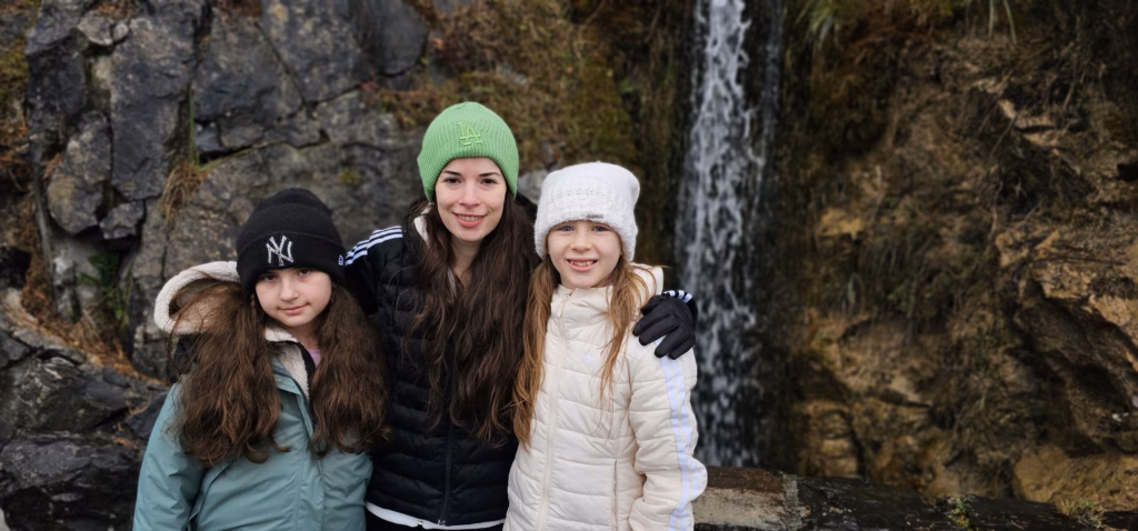 Samira in a green beanie with her arms around Lulu and another girl in front of the St. Beatus waterfall