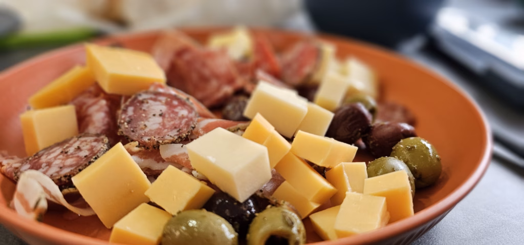 A terracotta plate of cubed cheese, salami slices and green and dark olives on the trailer table
