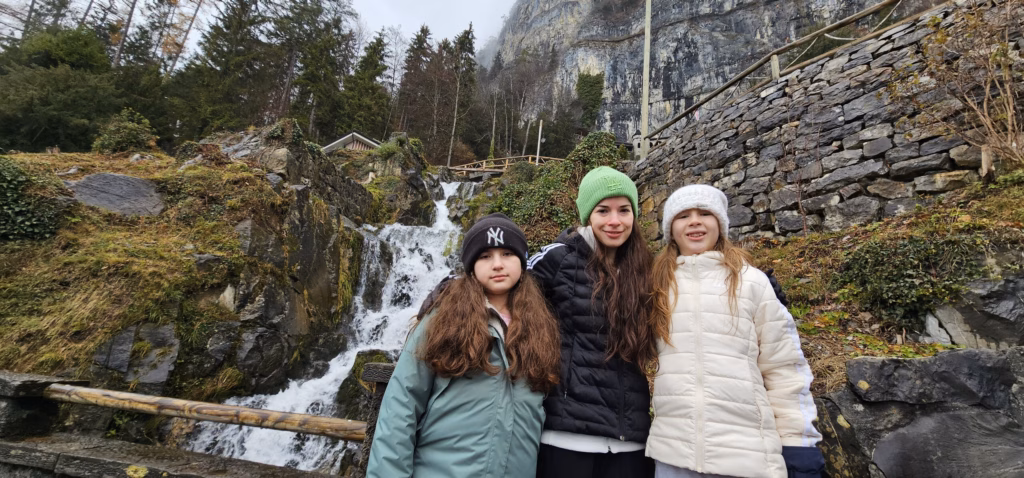 Samira with Lulu and Sahryah standing below the rocky cliff and the cascading Beatusbach waterfall
