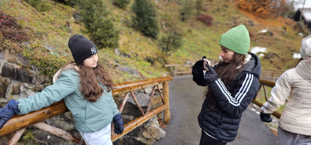 Samira in a green beanie photographing Lulu, who leans on a wooden railing on the gorge path
