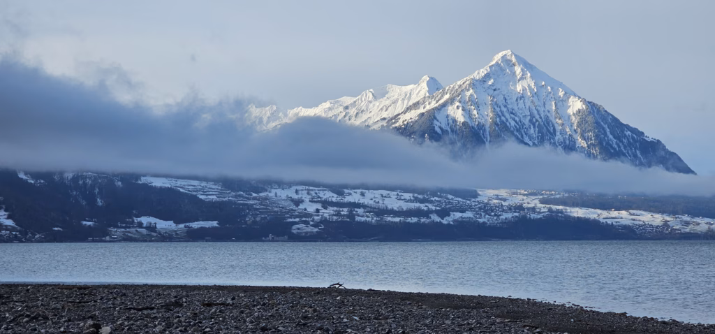 The snow-capped pyramidal Niesen peak catching morning sun over a calm Lake Thun