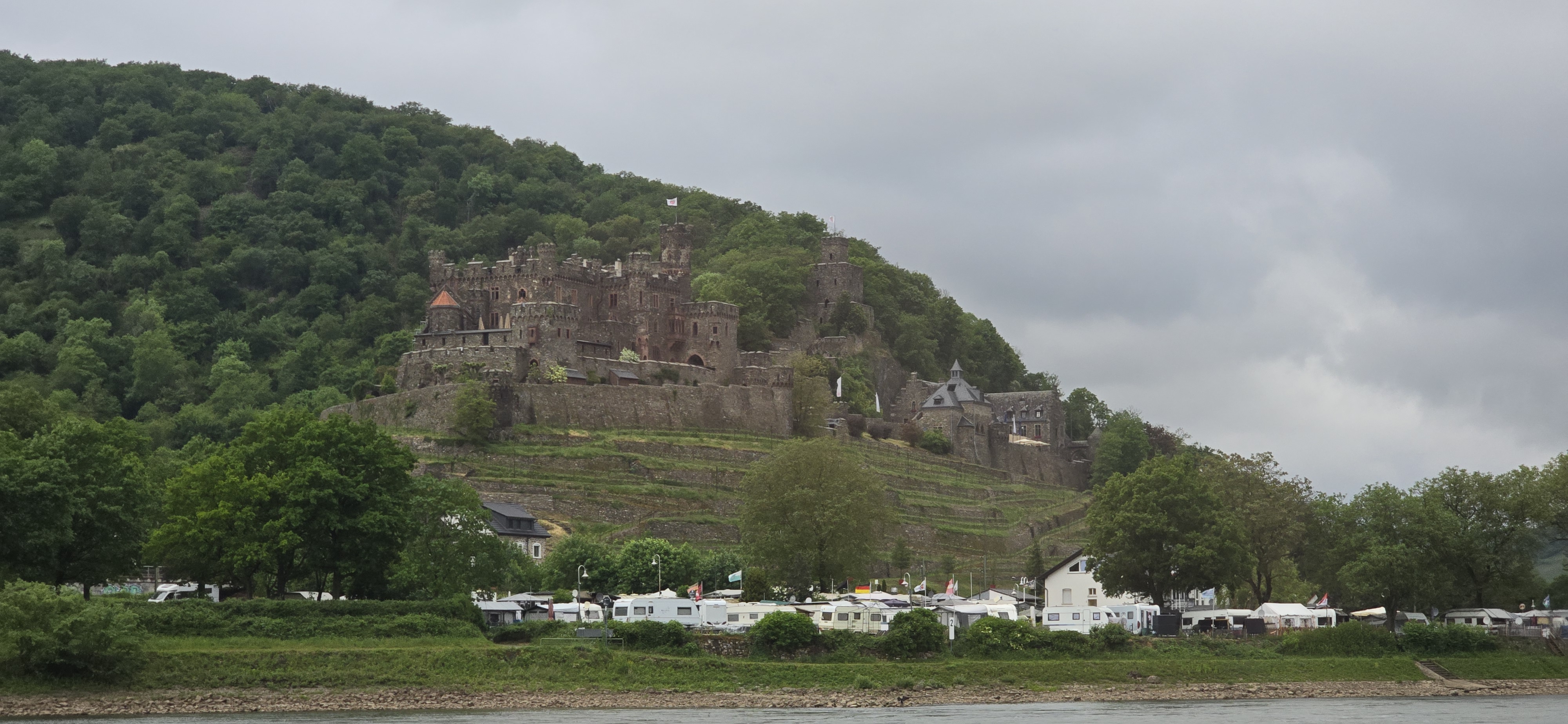 Burg Reichenstein above Trechtingshausen on the right bank of the Rhine, the campsite caravans still visible along the riverbank as the cruise boat passes