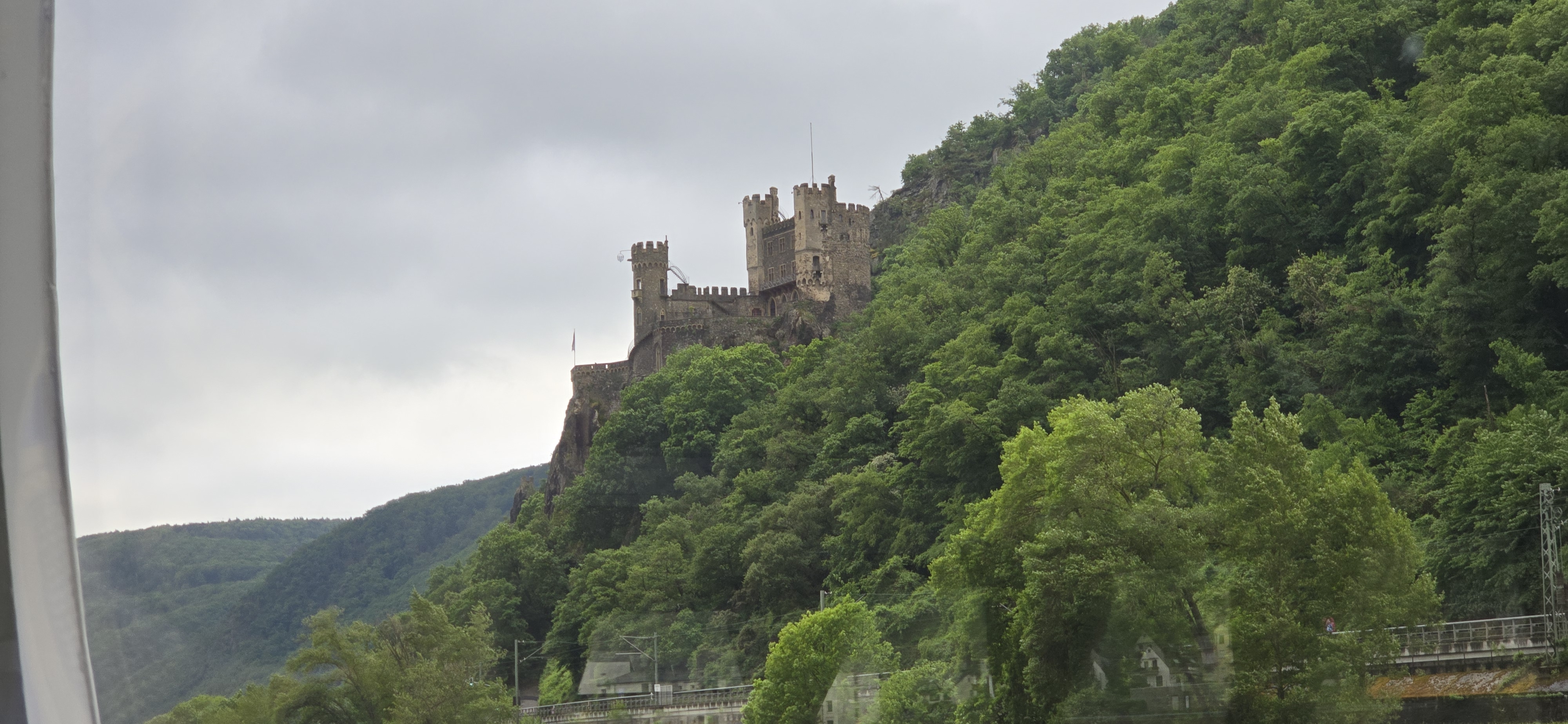 Burg Rheinstein on the wooded ridge near Trechtingshausen seen through the cruise boat window as the boat approaches Bingen