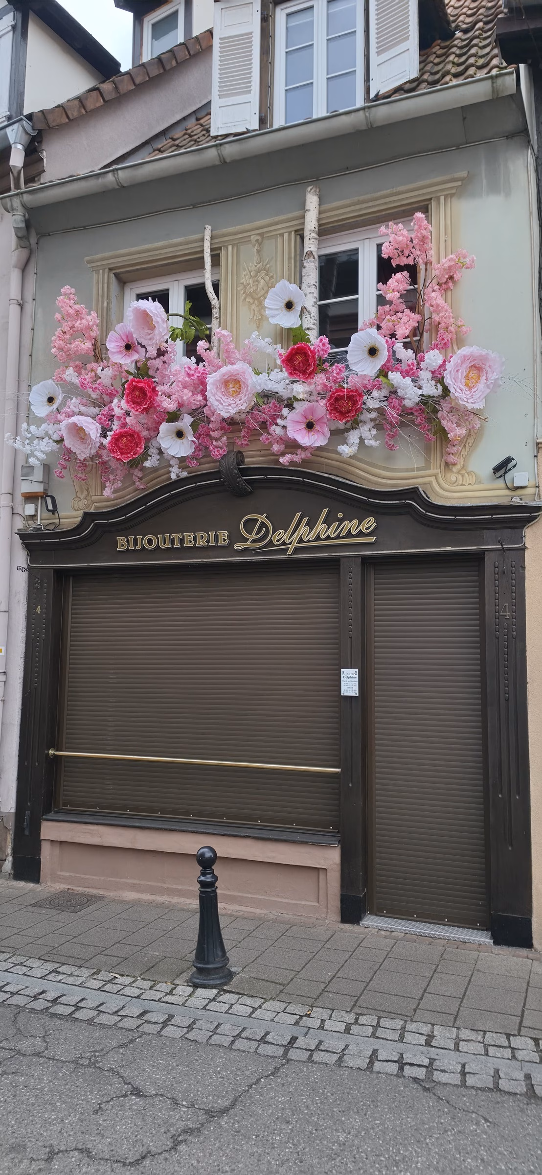 Bijouterie Delphine jewelry shop in Wissembourg with the morning flower display set out and the steel security shutter still down