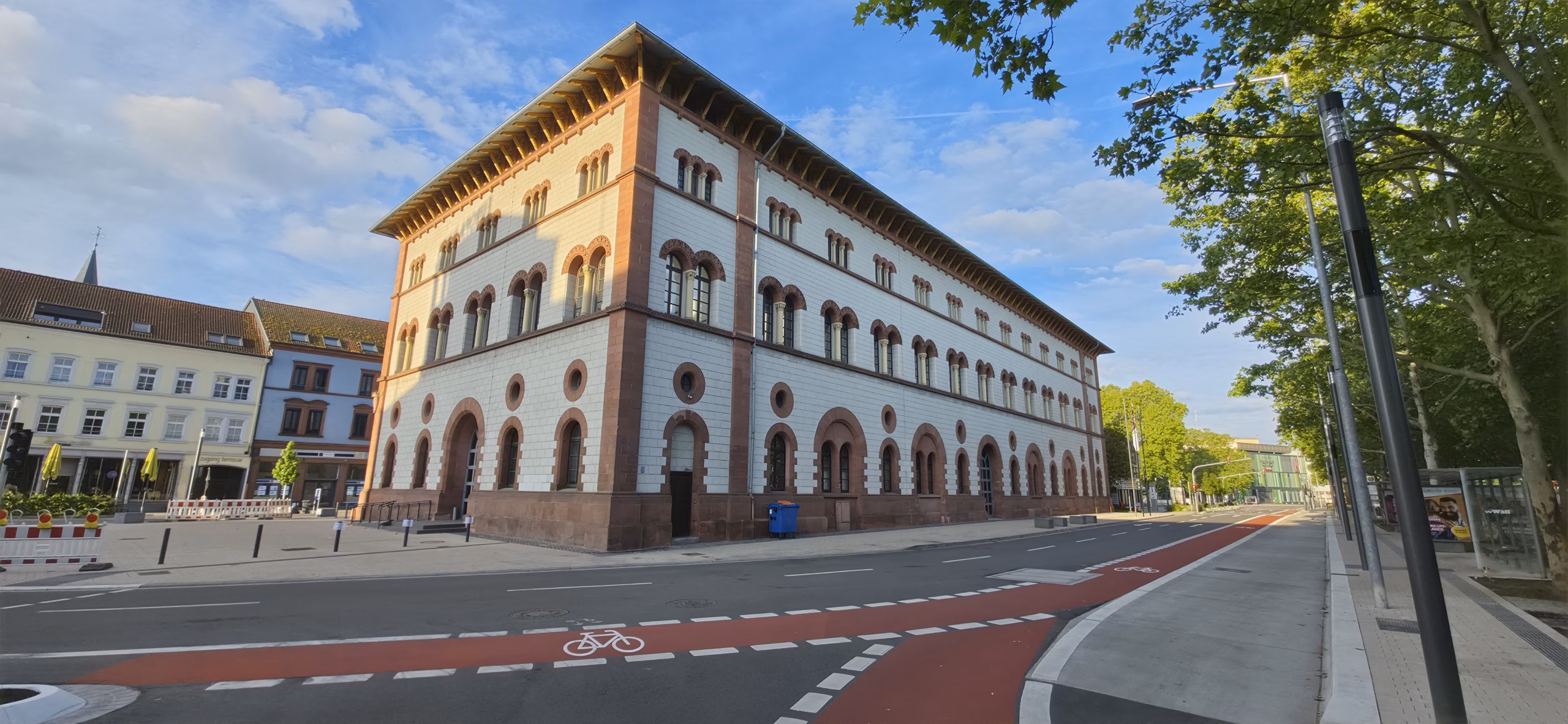 Golden-hour light on a sandstone civic building in the Kaiserslautern Altstadt, empty cobbled street with bike-lane markings in the foreground