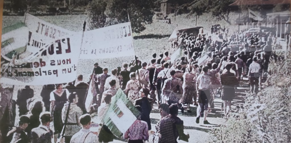 Reproduction on an information panel of a 1950 photograph showing European federalist students marching with cloth banners at the Sankt Germanshof border crossing
