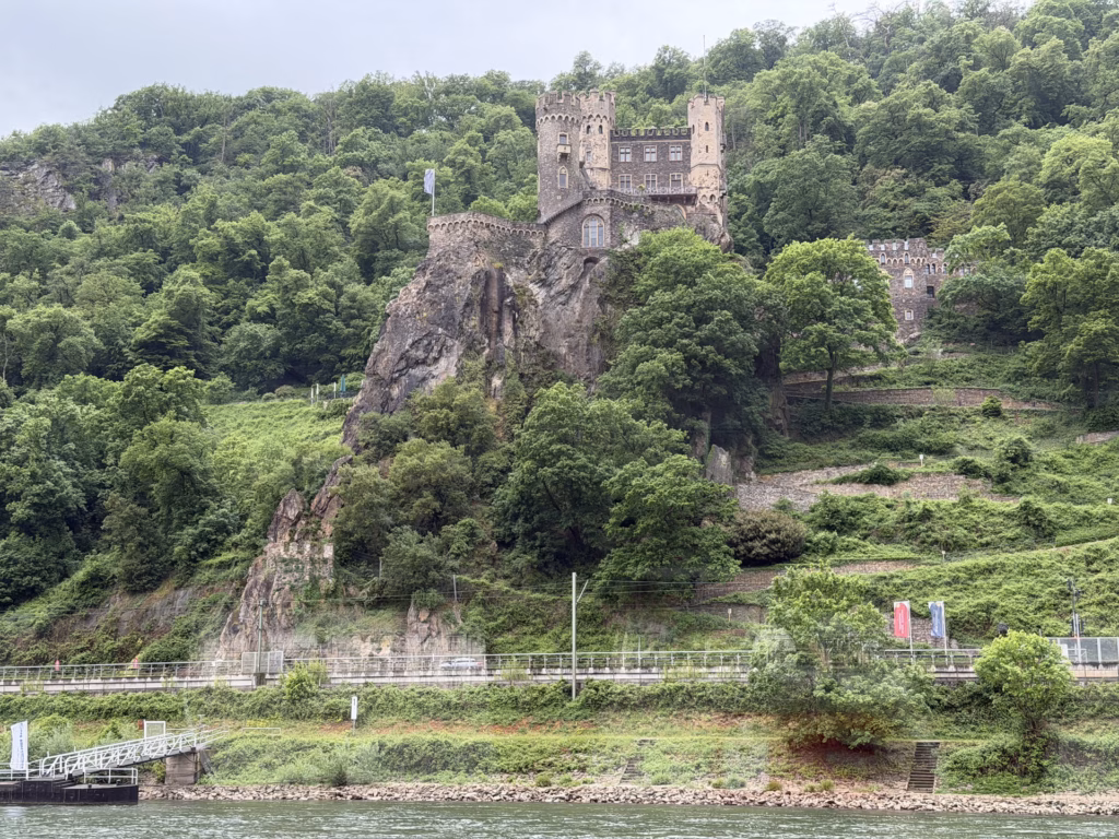 Burg Rheinstein perched on a steep rocky crag above the Rhine with terraced vineyards, seen from the boat near Bingen