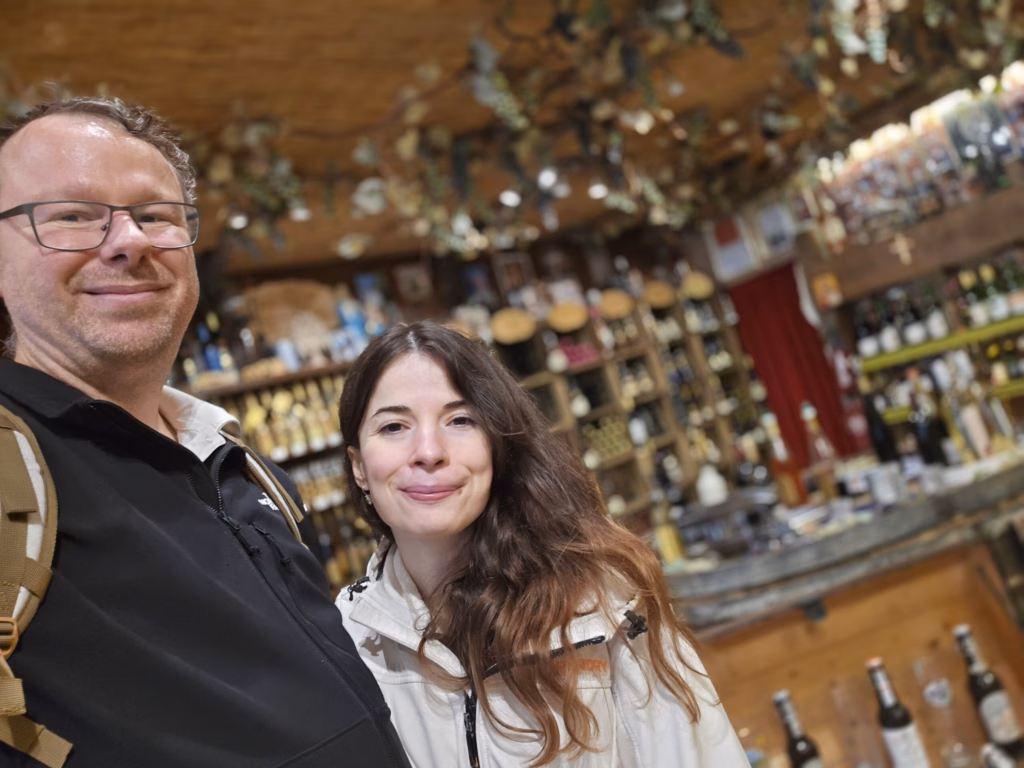Ryan and Samira taking a selfie inside Stefan's shop with bottle racks and greenery covering the ceiling