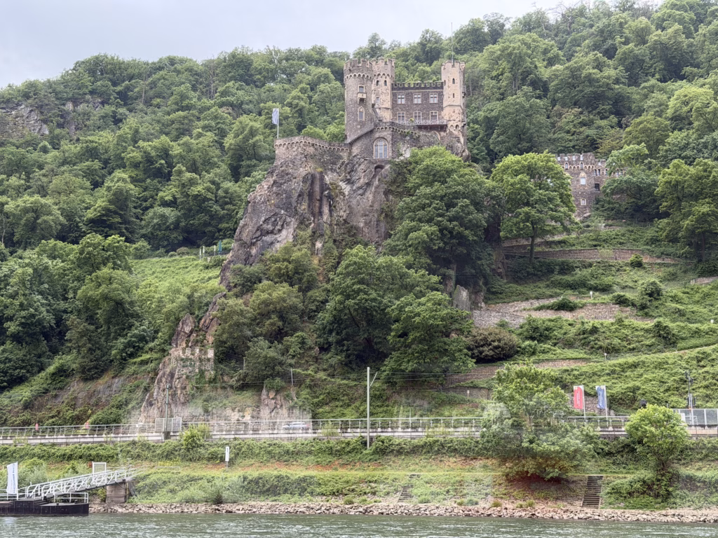 Burg Rheinstein perched on a steep rocky crag above the Rhine with terraced vineyards beside it