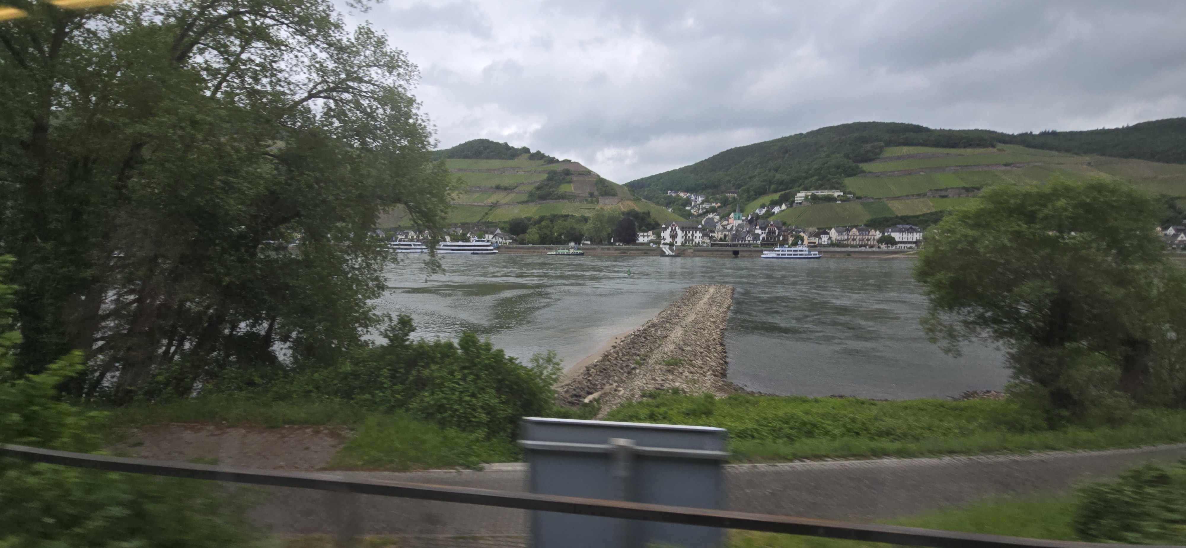 Rhine riverbanks with right-bank vineyards and cruise ships viewed from the RB26 train window approaching Bacharach