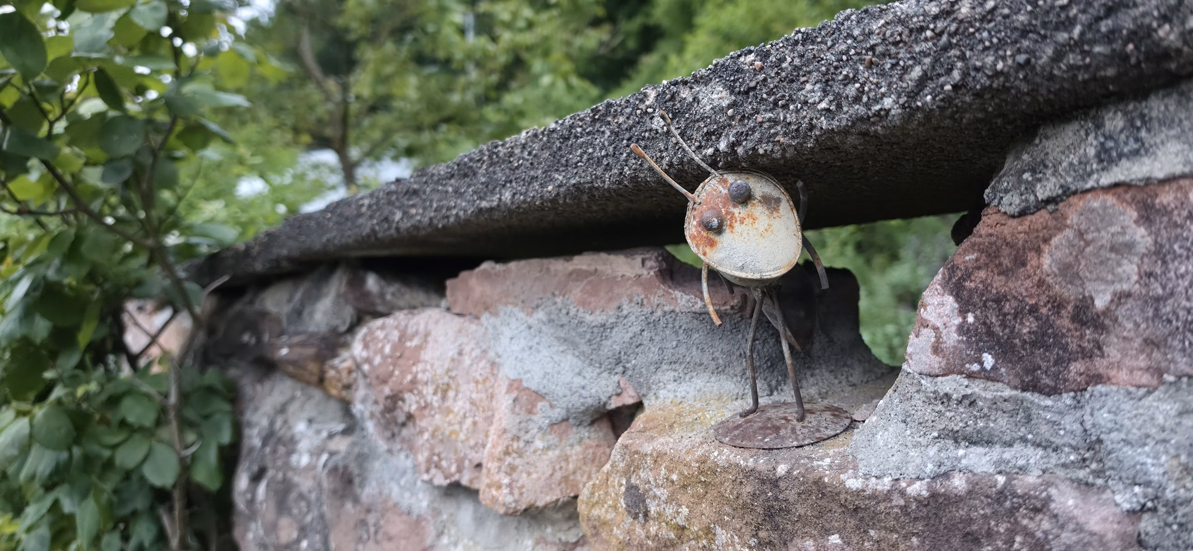 A rusted metal critter sculpture welded onto a sandstone garden wall in the hamlet of Sankt Germanshof