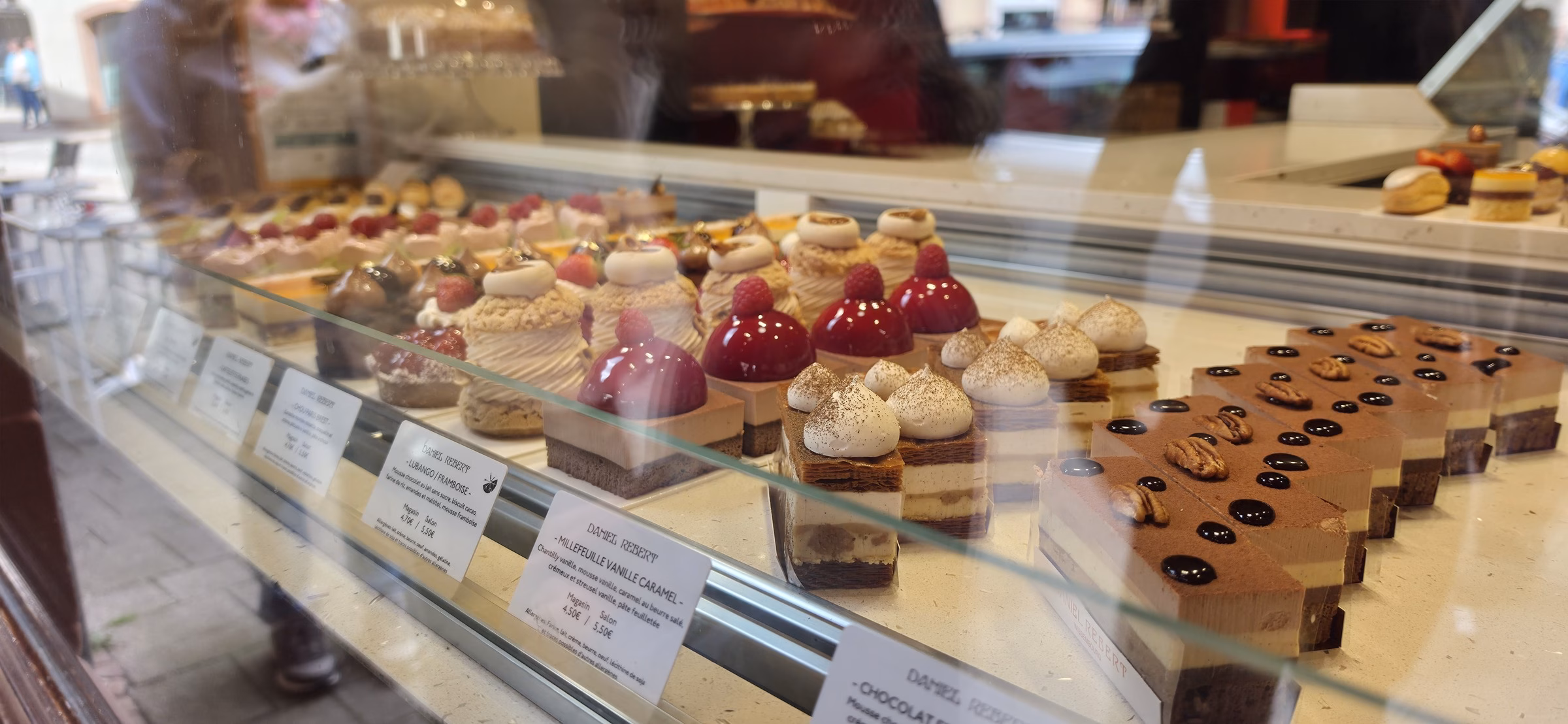 The Daniel Rebert pastry display case in Wissembourg with rows of millefeuille, raspberry tarts, chocolate domes, and other signature petits gateaux