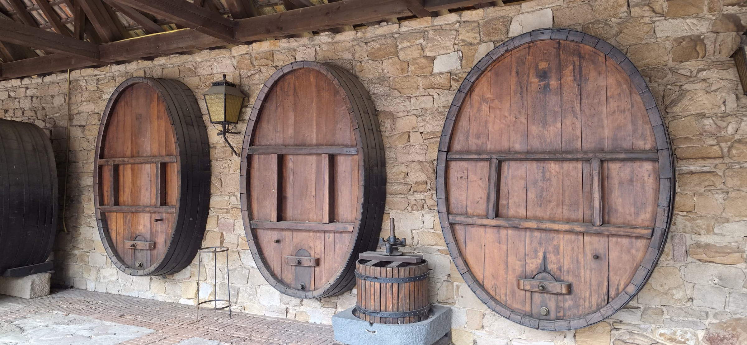 Three large Fuder wine barrels mounted on the stone wall of the Weintor cellar in Schweigen, with a traditional wine press in front