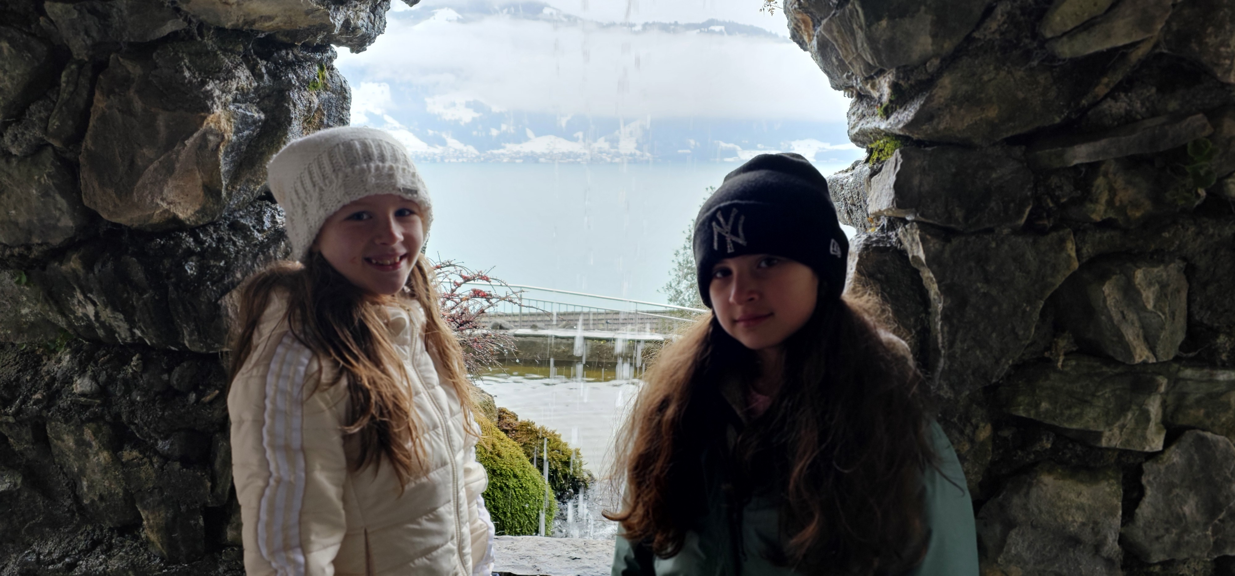 Lulu and Sahryah framed inside a stone arch on the cave-park grounds, with Lake Thun visible through the opening