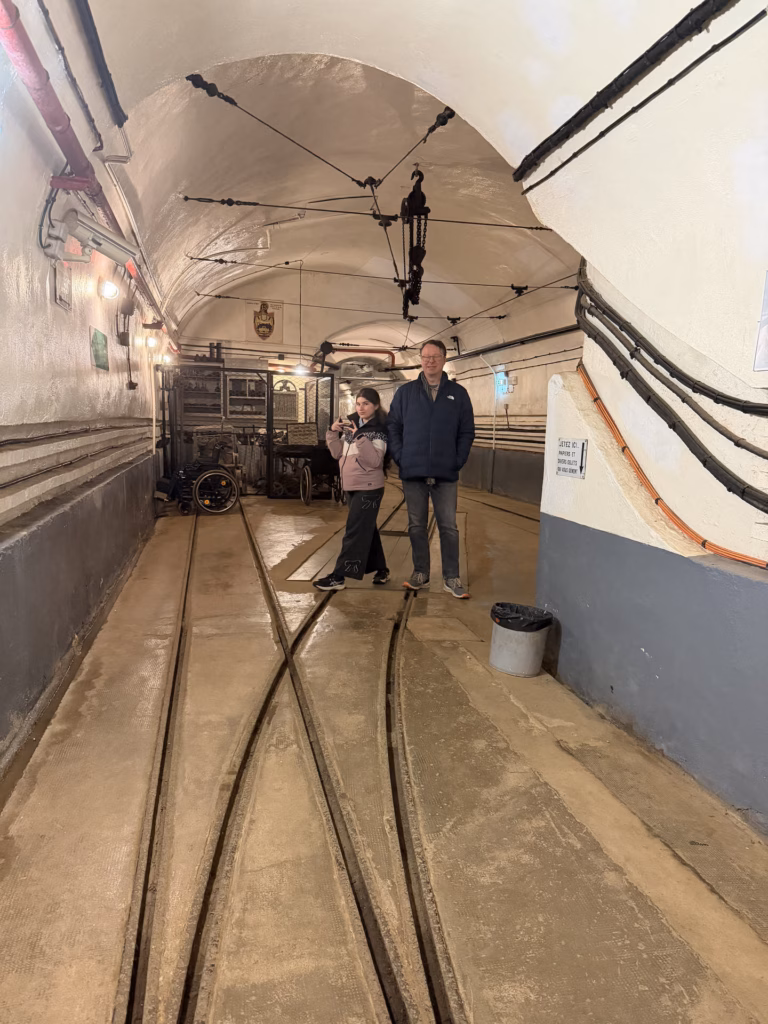 Ryan and Lulu standing in the main underground gallery of the fort with floor rail tracks and overhead lines receding into the distance