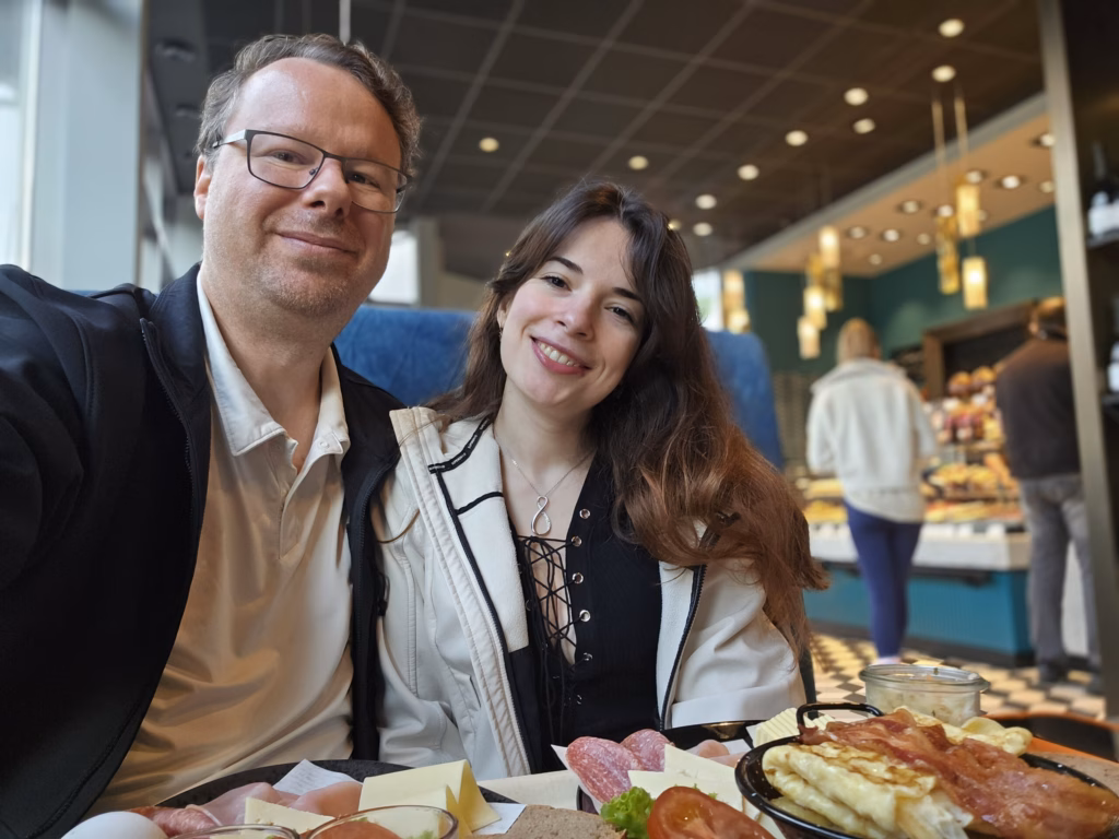Ryan and Samira taking a selfie at a bakery cafe table with the breakfast spread in front and the counter behind