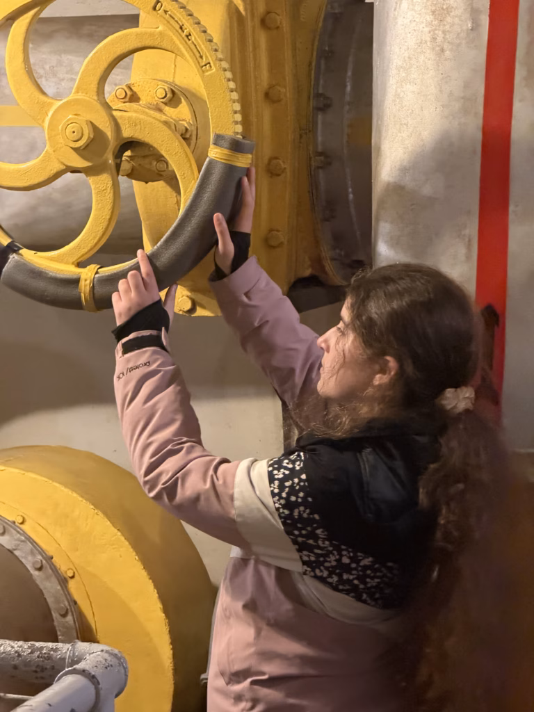 Lulu reaching up to turn a large yellow valve wheel on the fort's machinery