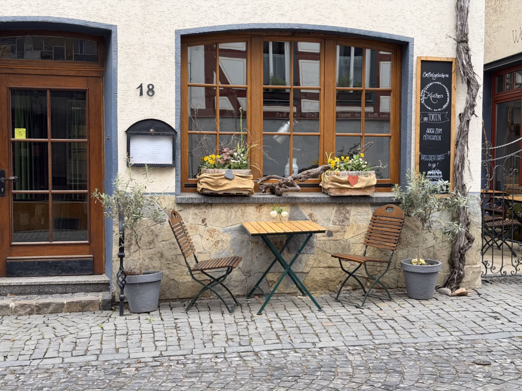 A small bistro table and chairs on the cobbles in front of a half-timbered house numbered 18 in Bacharach