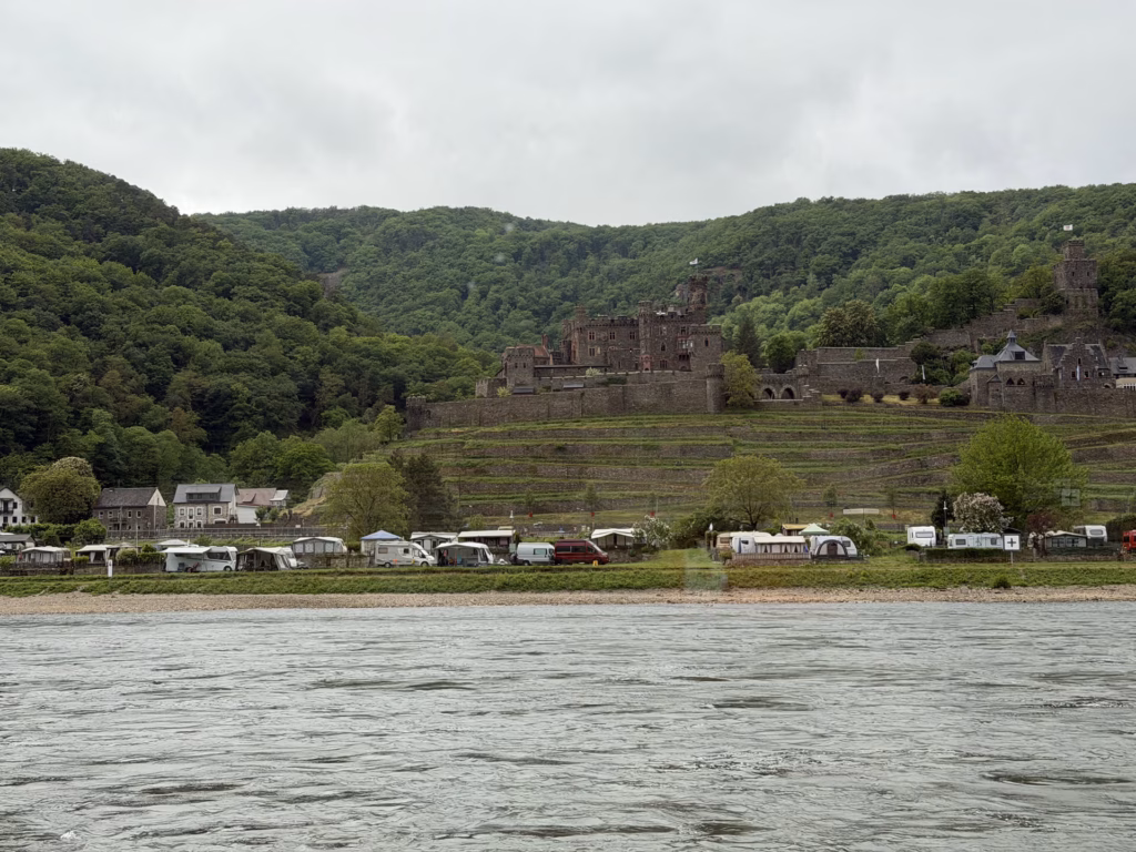 Burg Reichenstein on the wooded hillside above a riverside campground, seen from the Rhine