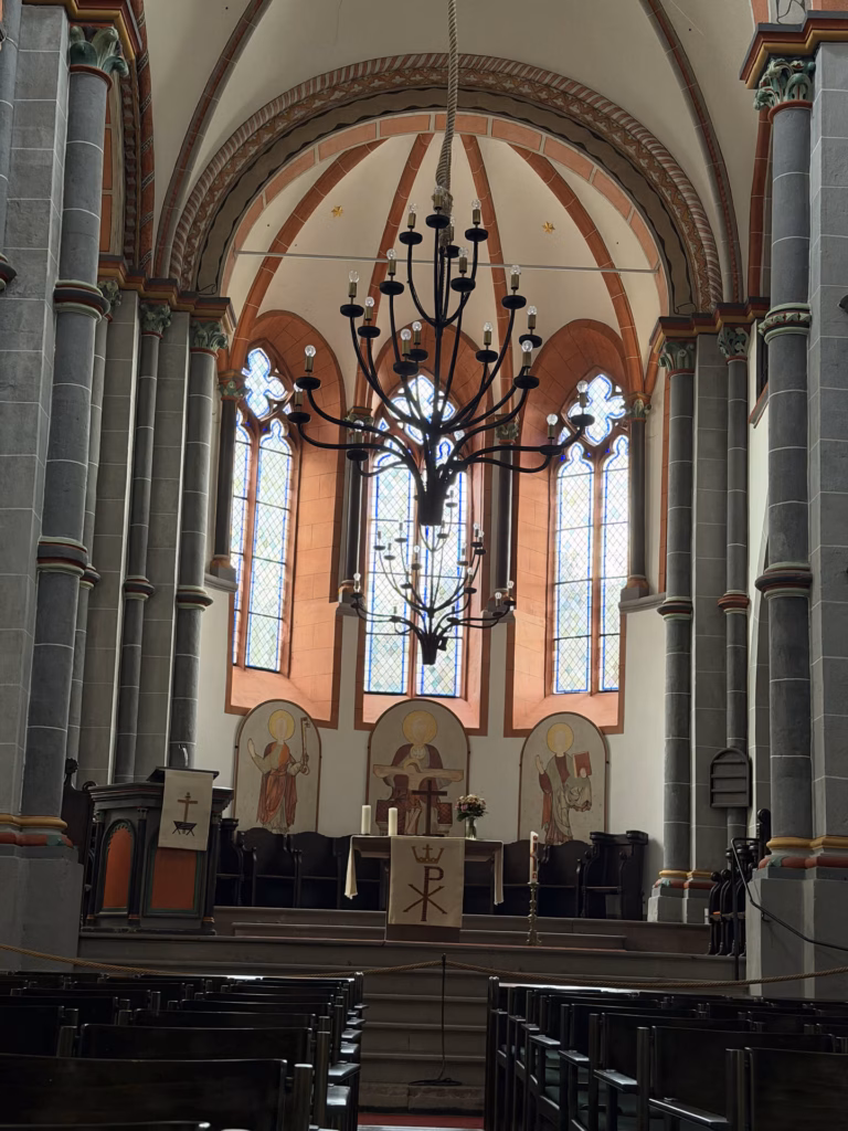 The pink and ochre Gothic nave of St. Peter church in Bacharach with a chandelier and altar