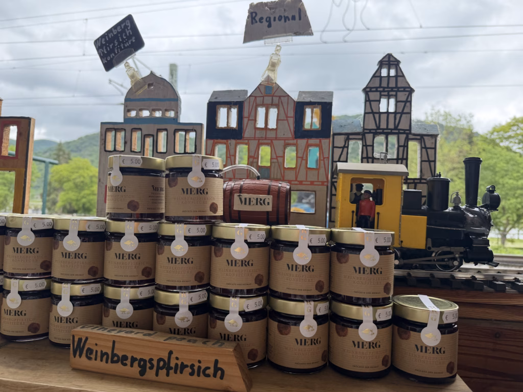 A wine-shop window display of Weinbergspfirsich jars stacked around a model-town diorama with a toy steam train