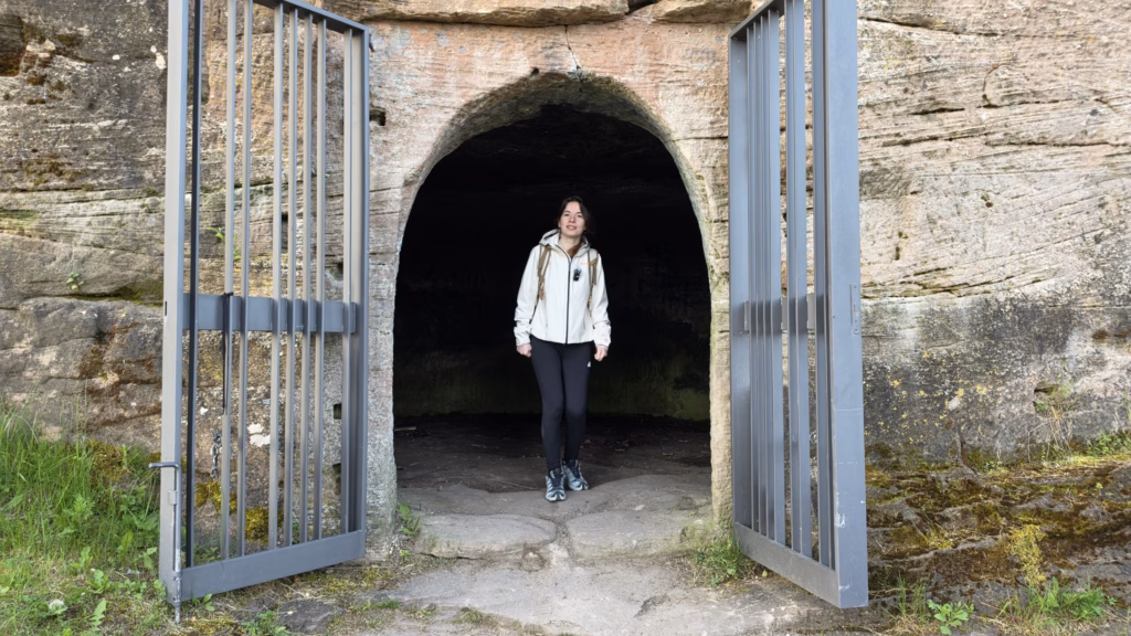 Samira standing in a rock-cut sandstone chamber doorway with the iron gates open