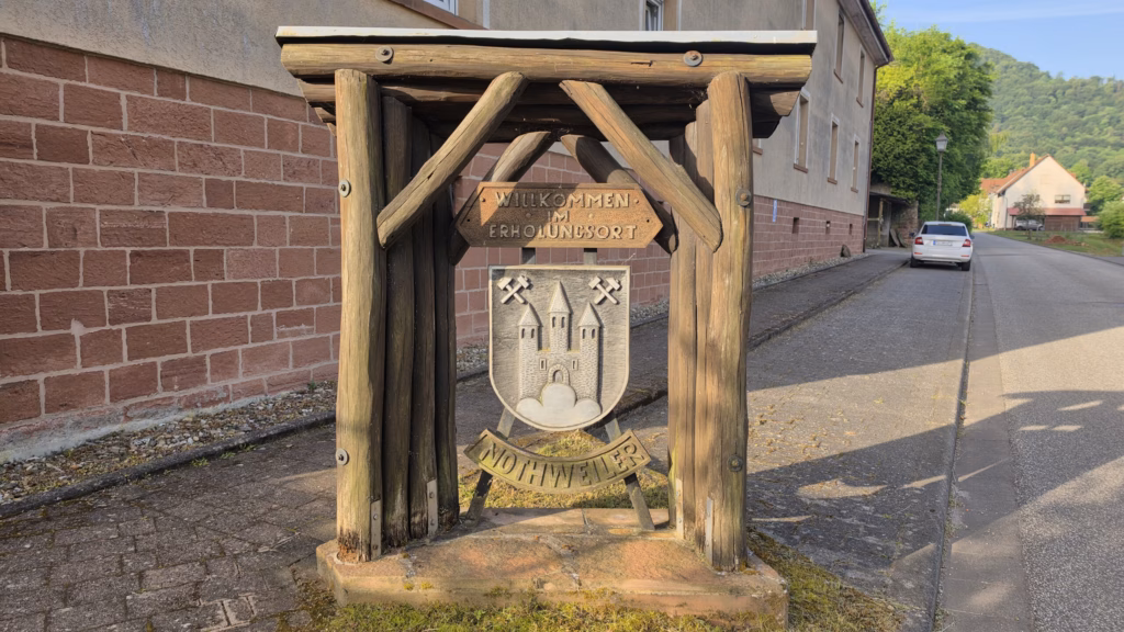 Nothweiler Ortseingangsschild with the Wegelnburg in its crest, back in the village in morning sun